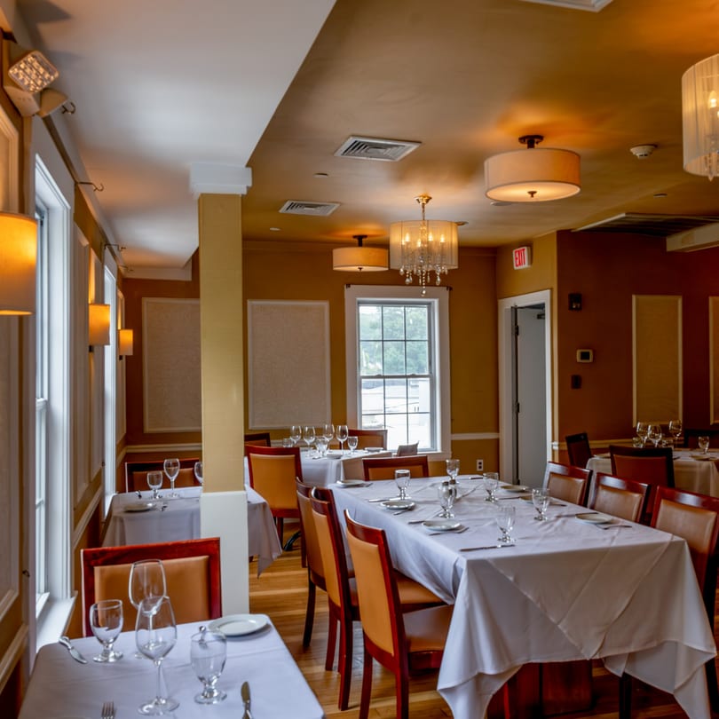 Elegant Tartufo Restaurant dining room with set tables, warm lighting, and large windows.