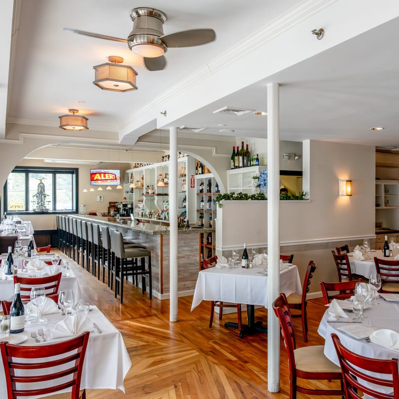 Tartufo Restaurant's dining room with set tables, red chairs, and a full bar area.