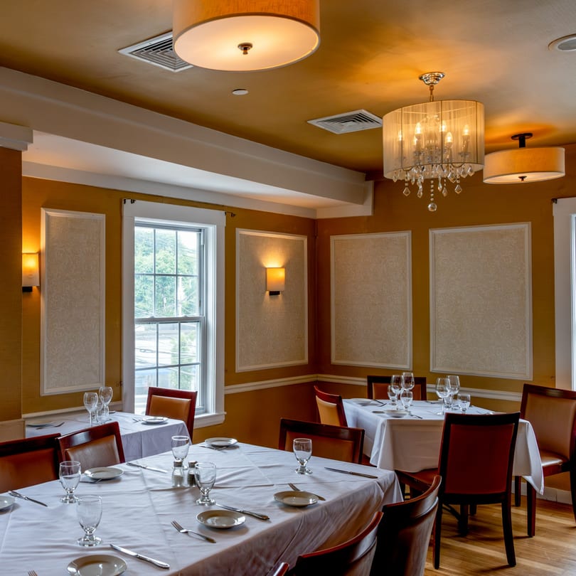 Elegant dining room at Tartufo Restaurant with set tables, chandeliers, and warm lighting.