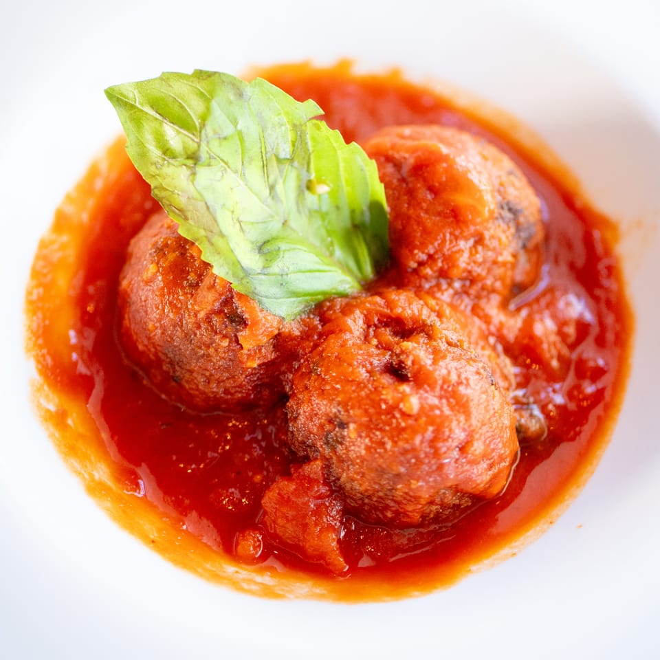 Three Italian meatballs in rich red tomato sauce, garnished with a fresh basil leaf.