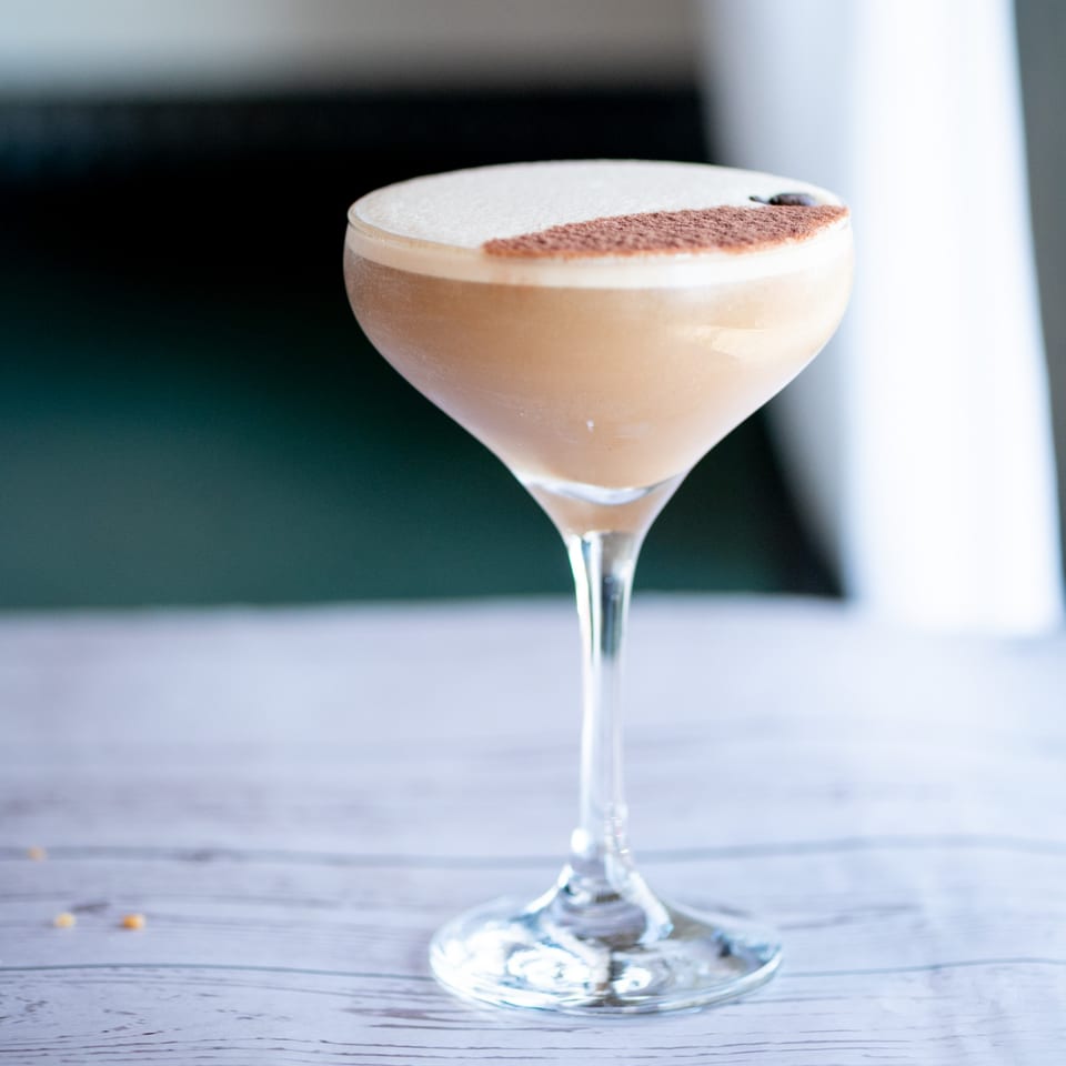 A creamy cocktail with foam and a dusting of cocoa powder in a martini glass.