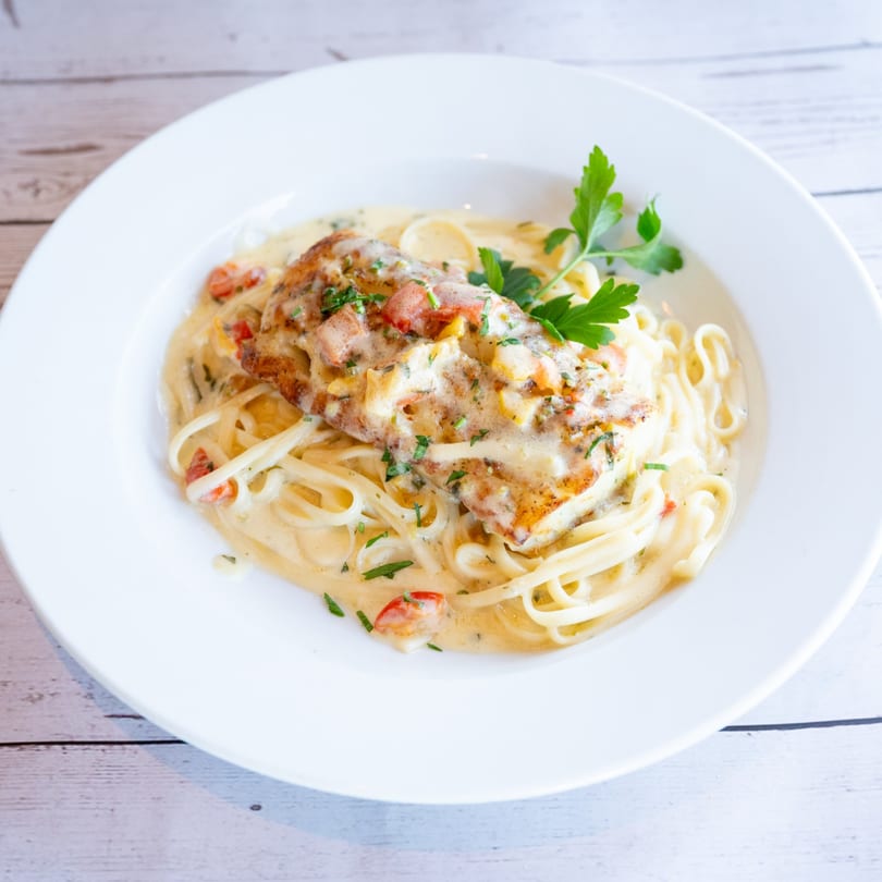 Creamy Italian pasta dish with chicken, tomatoes, and parsley in a white bowl.