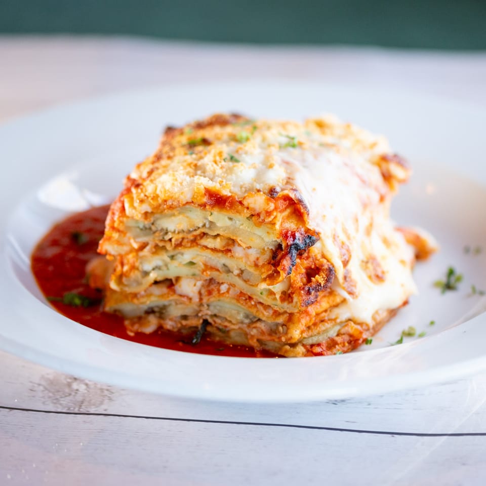 A close-up of a delicious, layered Italian lasagna with melted cheese and red sauce on a white plate.