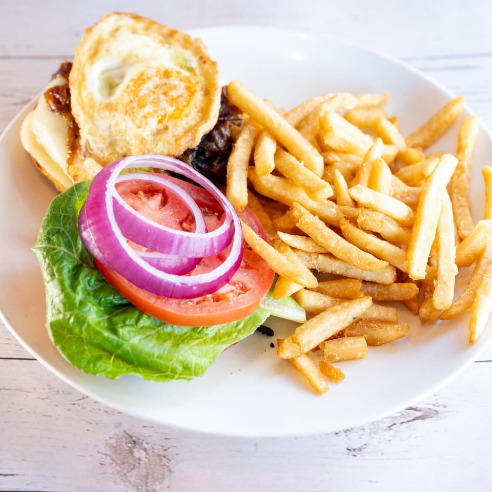 A burger with a fried egg, cheese, lettuce, tomato, and red onion, served with fries.