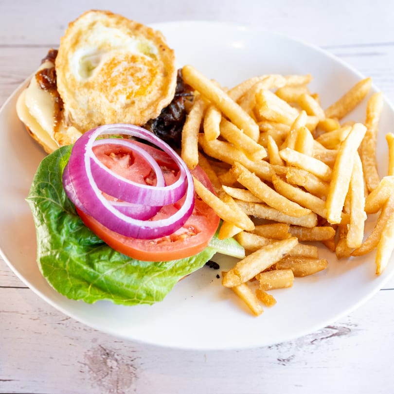 A burger with a fried egg, cheese, lettuce, tomato, and red onion, served with fries.