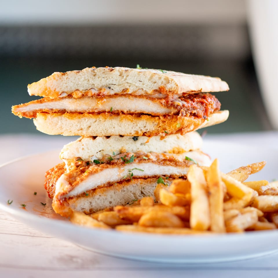 Tartufo Restaurant's chicken parmesan sandwich, cut in half, with a side of golden french fries.