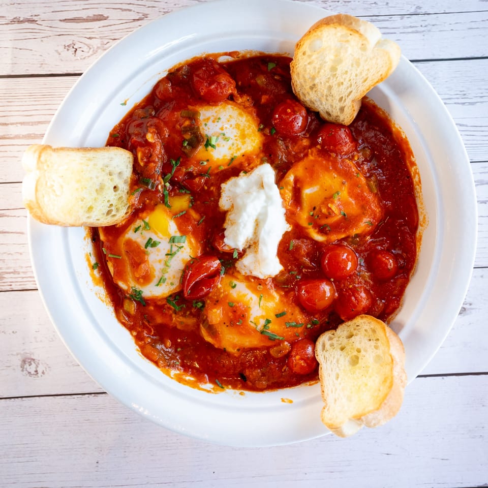 Shakshuka with poached eggs, rich tomato sauce, fresh herbs, and toasted bread on a white plate.