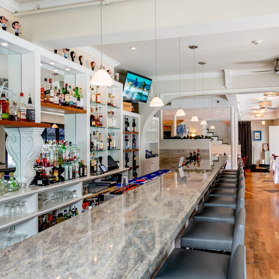 Long, well-stocked bar with a granite top and gray stools, leading to a dining area.