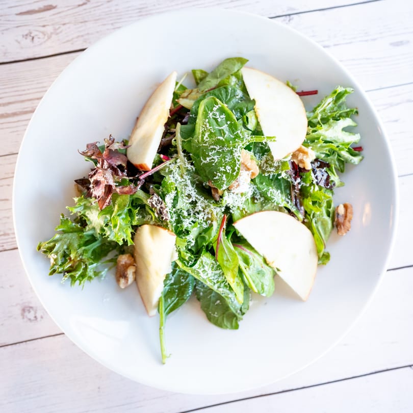 Fresh Italian salad with mixed greens, apple slices, walnuts, and grated cheese on a white plate.
