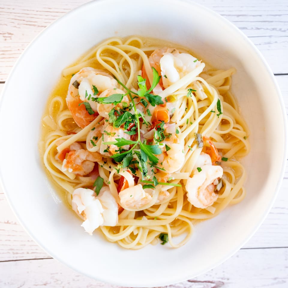 Tartufo Restaurant's shrimp scampi with linguine pasta, garlic, parsley, and a light sauce in a white bowl.