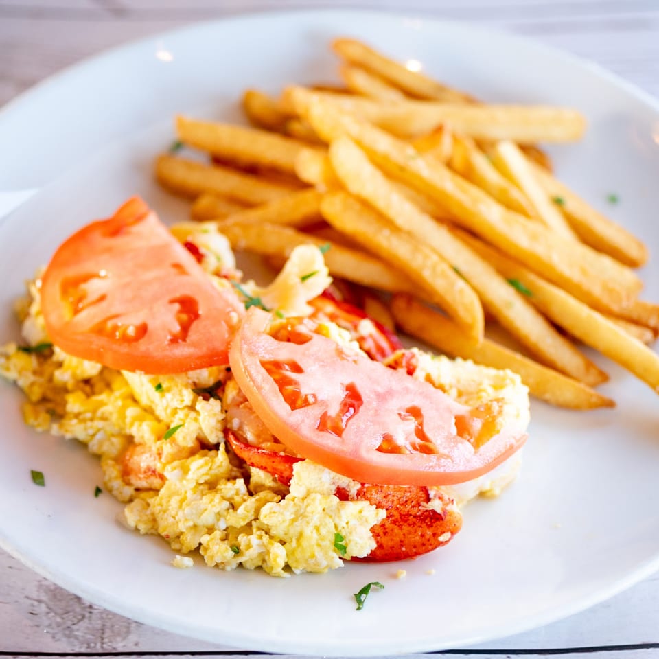 Scrambled eggs with lobster and tomato slices, served with a side of golden french fries.