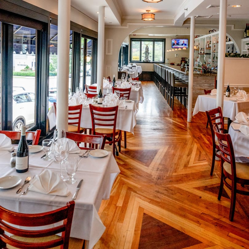 Tartufo Restaurant's dining room with set tables, a bar, and large windows overlooking the street.